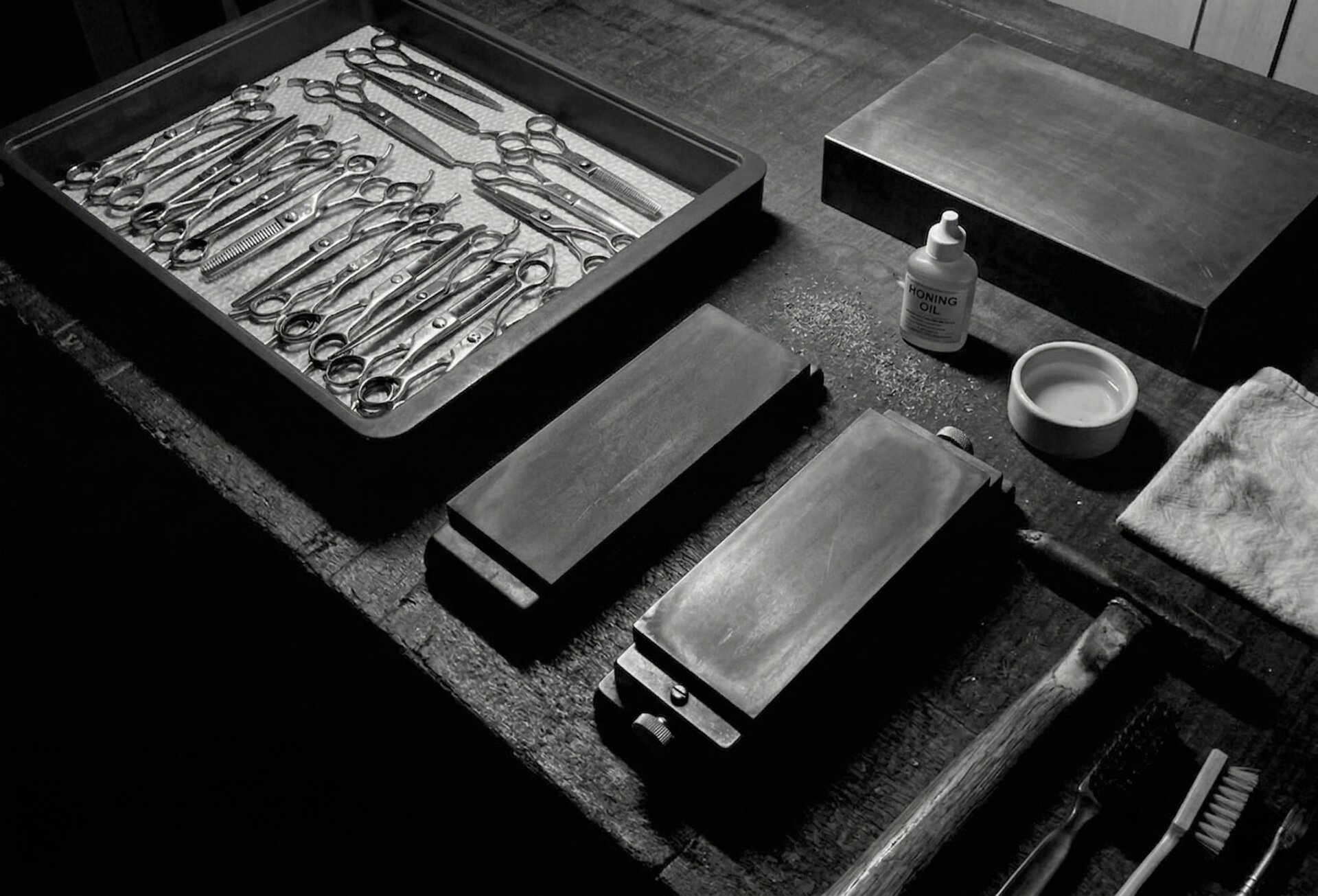 Professional scissors sharpening workshop with multiple shears and maintenance stones arranged on dark surface