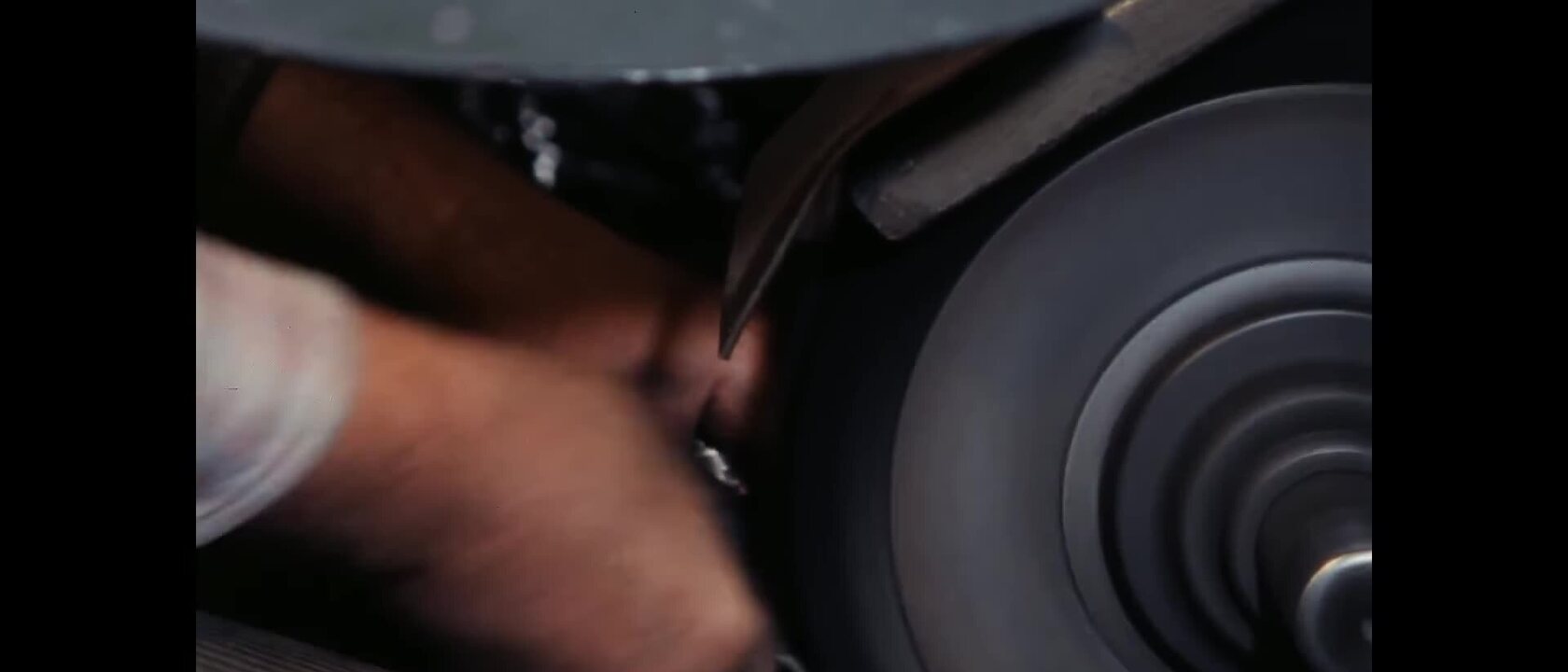 Close-up of a Solingen craftsperson holding a scissor part against a rotating polishing wheel