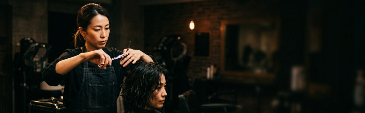 Female barber cutting male customer with dark theatrical lighting
