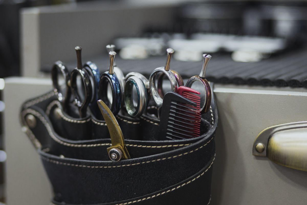 Several professional shears and combs stand in a leather barber-tool holster.
