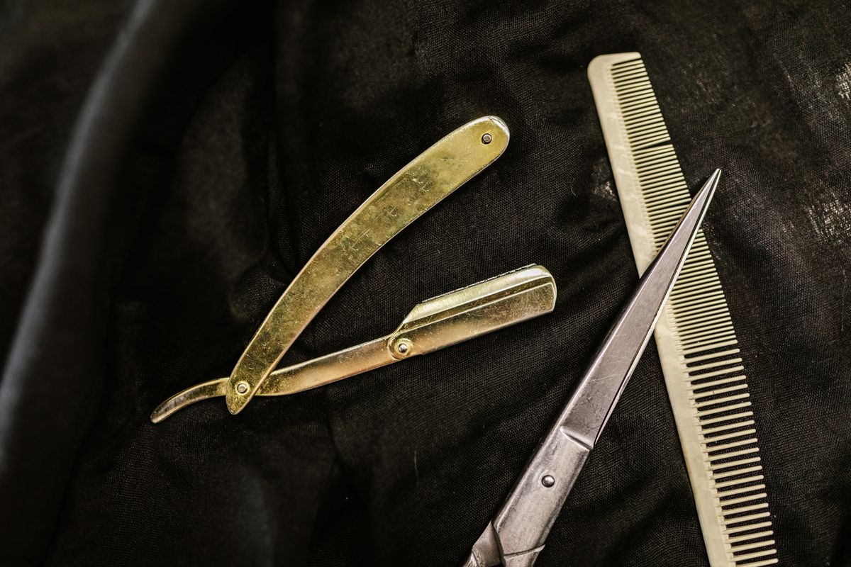 A professional cutting shear, comb, and straight razor lie on black cloth.