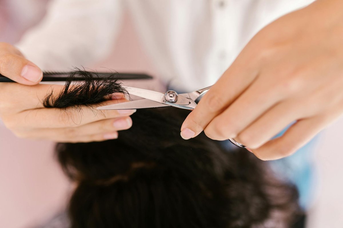 En stylist bruger en sølvfarvet klippesaks på en sektion af mørkt hår.