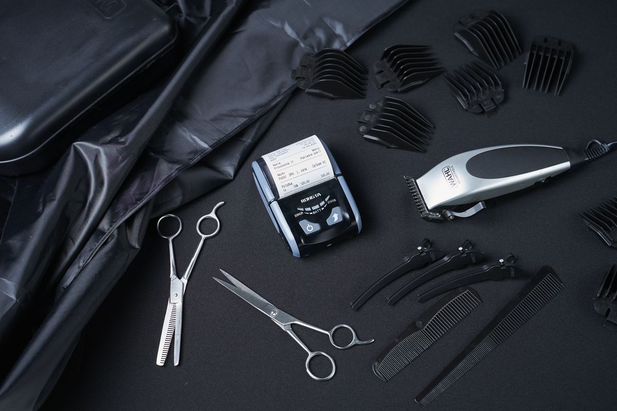 Cutting shears, clippers, guards, combs, and a receipt printer lie on black cloth.