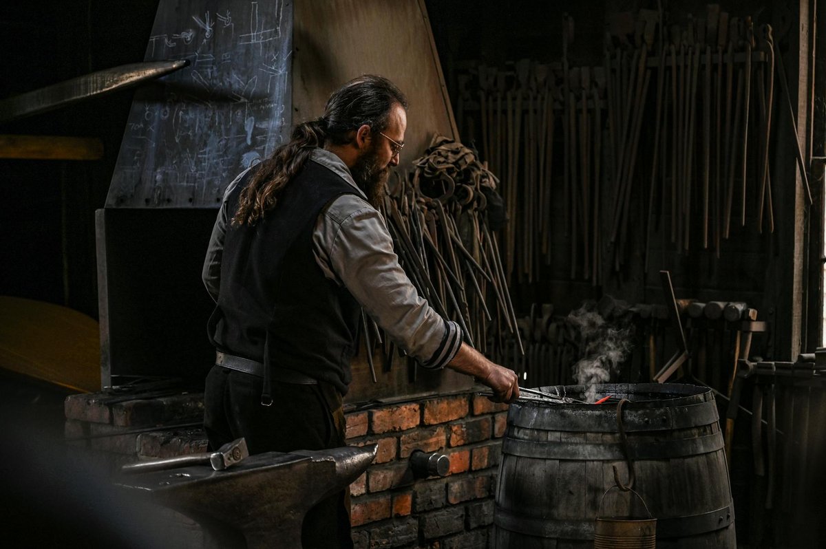 A blacksmith works metal with traditional tools in a rustic workshop.