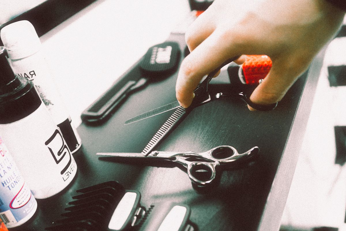 A hand reaches toward cutting and toothed shears on a salon workstation.