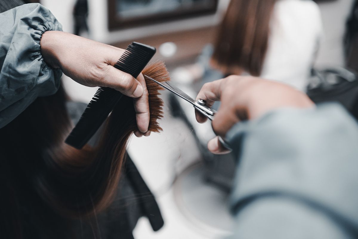 En stylist trimmer en brun hårseksjon med en klippesaks og svart kam.