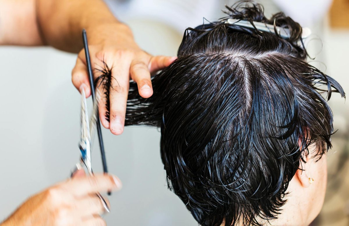 A stylist uses a silver shear and black comb while cutting short wet hair in a salon
