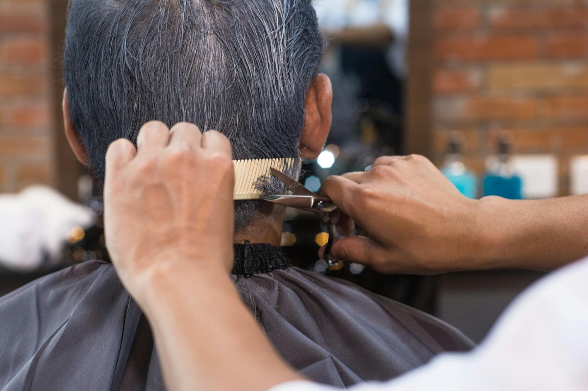 A barber trims short hair with a cutting shear held over a comb.