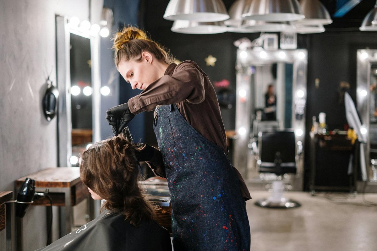 A stylist leans over a seated client while working on their hair.