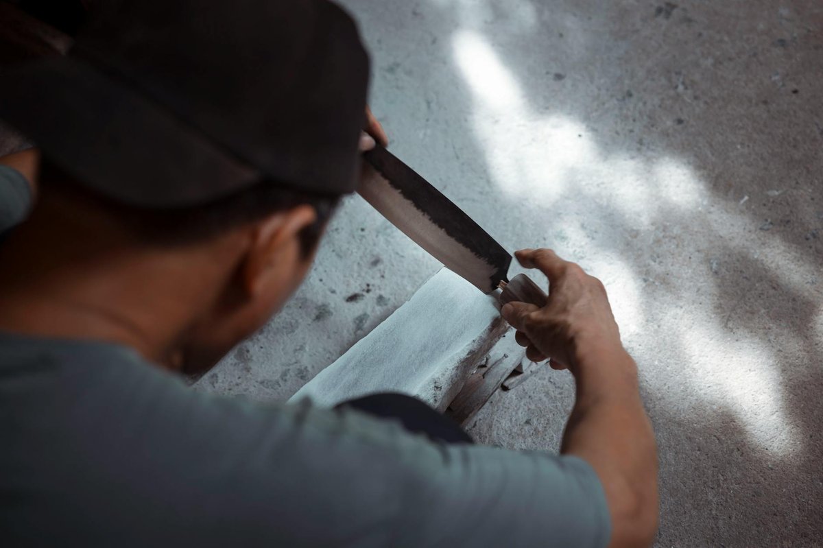 A man sharpens a knife blade on a whetstone in a traditional manner.