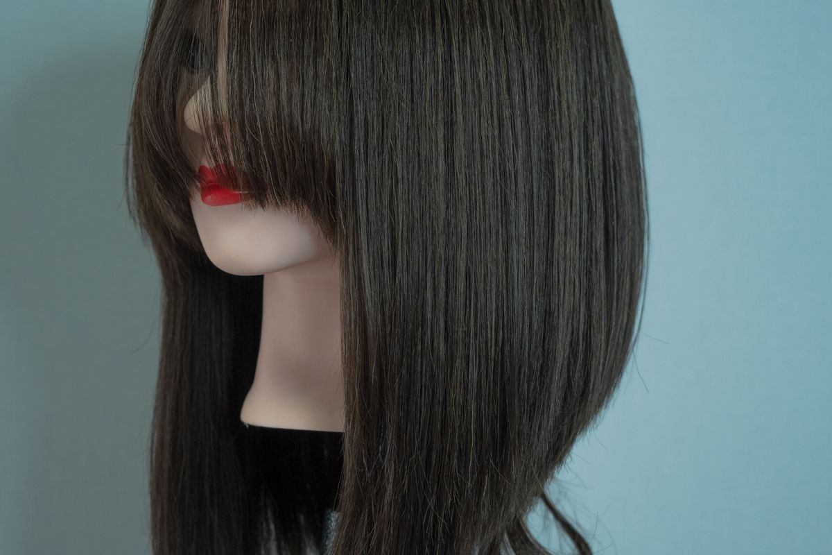 A long-haired training mannequin head stands against a plain background.
