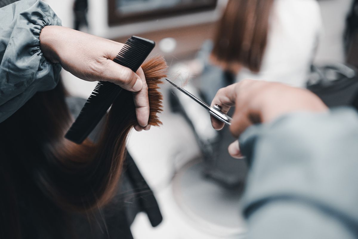 A close view shows hands using a cutting shear and comb on a hair section.