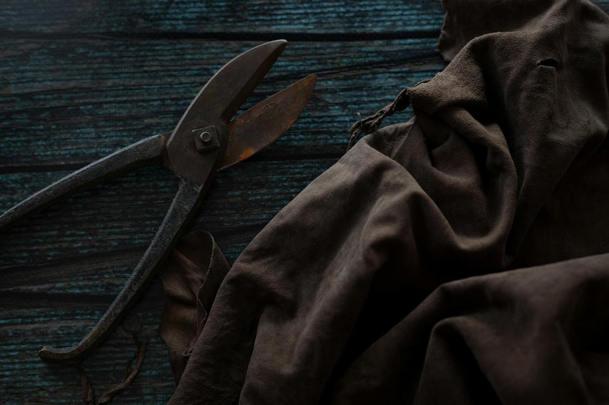 Vintage scissors and brown fabric rest on a dark wooden surface.