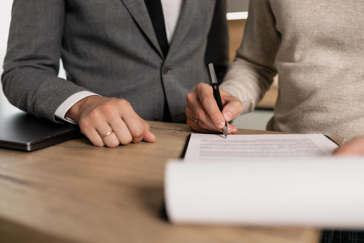 Two people review and sign a document together at an office table.